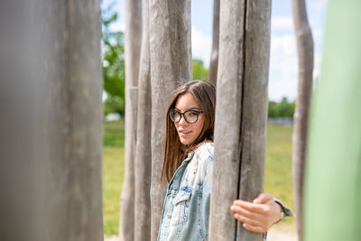 Portrait of young woman standing by tree trunk