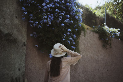 Rear view of teenage girl wearing hat while walking against wall