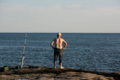 Rear view of shirtless man fishing in sea