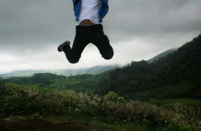 Low section of man jumping on mountain against sky