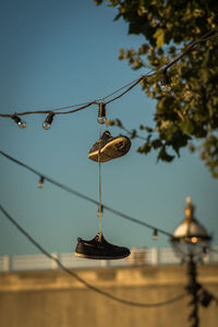 Low angle view of shoes hanging on cable against sky