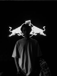 Portrait of young man standing against black background