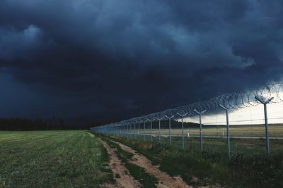 Fence on field against storm clouds