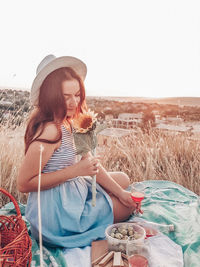 Young woman wearing hat sitting on field against clear sky