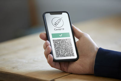 Man holding mobile phone with digital vaccination card over wooden table