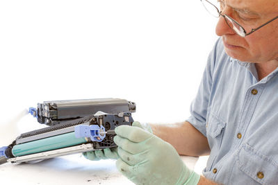 Close-up of man repairing cartridge against white background