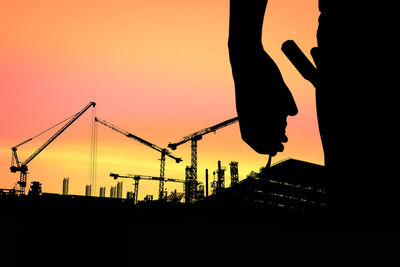 Silhouette cranes at construction site against sky during sunset