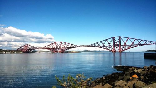 Firth of forth road bridge over river against blue sky on sunny day