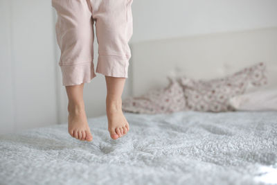 The child jumps on the bed, legs close-up, without a face. white and pastel colors, gentle toning