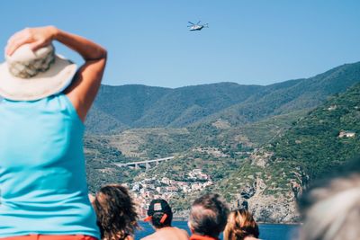 Rear view of people watching helicopter flying over mountain