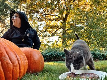 Full length of cat eating in field during autumn with person