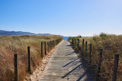 Wooden fence on footpath amidst field against clear sky