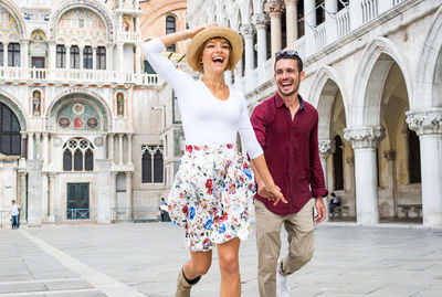 Cheerful young couple walking on street against cathedral in city