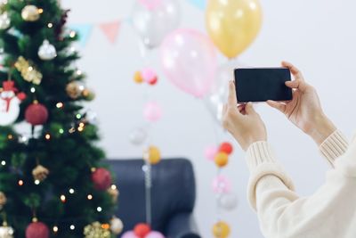 Midsection of woman holding smart phone at christmas tree
