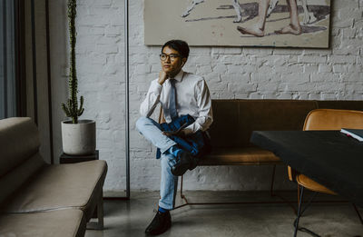 Businessman sitting over sofa with hand on chin at office