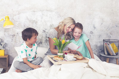 Cheerful mother with children having breakfast on bed