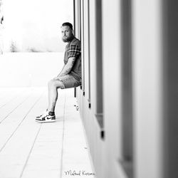 Young man looking away while sitting on wall