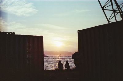 Silhouette buildings by sea against sky during sunset