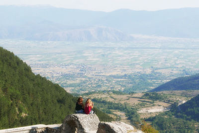 Rear view of people sitting on mountain against sky