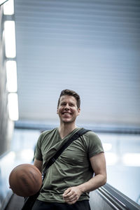 Low angle view of young man playing with basketball while moving down on escalator