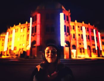 Portrait of smiling woman standing against illuminated building at night