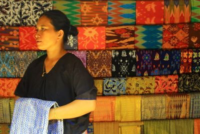 Woman looking away while standing against variety of textiles at market