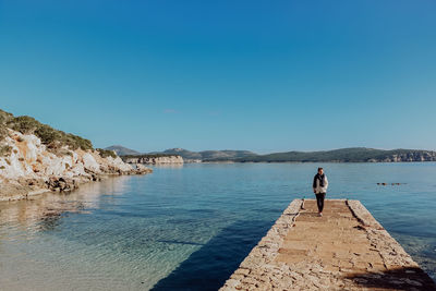 Woman walking on pier over sea against clear blue sky