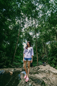 Full length of woman standing on rock in forest