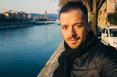 Portrait of handsome man standing by river against sky