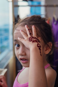 Portrait of henna ornaments on little girl's hand covering face.