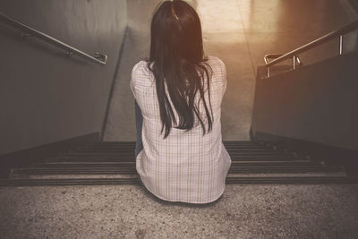 Rear view of woman sitting on stairs