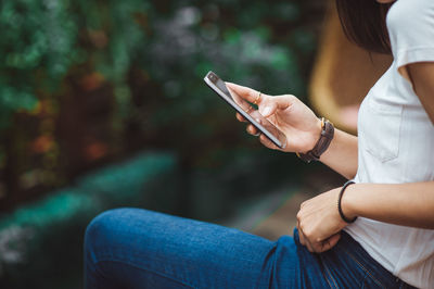 Midsection of woman using mobile phone while sitting outdoors