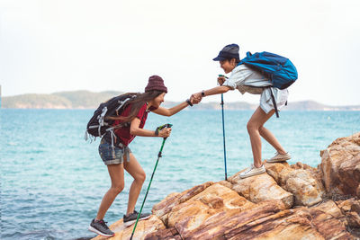 Boys standing on rock by sea against sky