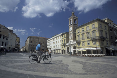 People riding bicycle on street amidst buildings in city