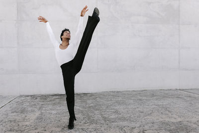 Flexible male dancer looking up while stretching leg against wall