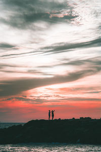 Silhouette people standing on shore against sky during sunset