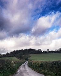 Road passing through field against cloudy sky