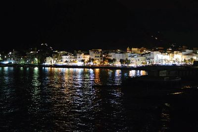 Illuminated cityscape by river against sky at night