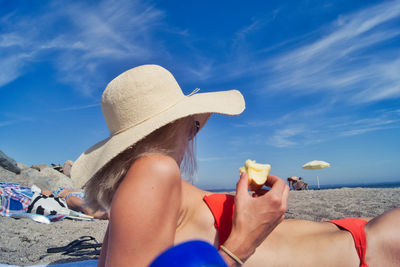 Woman holding apple at beach against sky