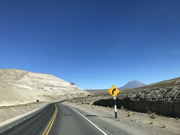 Road leading towards mountains against clear blue sky