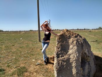 Woman standing by rock on field against clear blue sky