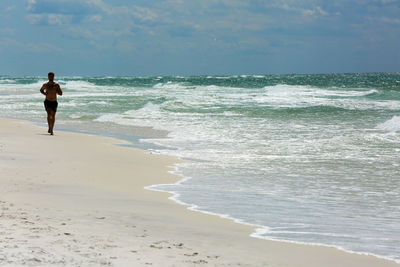 Man running on beach against sky