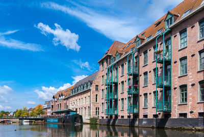 View of buildings by river against cloudy sky