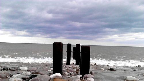Wooden posts on beach against cloudy sky