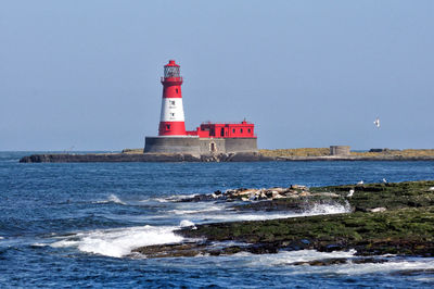 Lighthouse by sea against clear sky