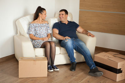 Full length of couple sitting on sofa at home