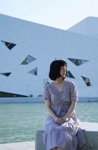 Woman sitting by sea against sky