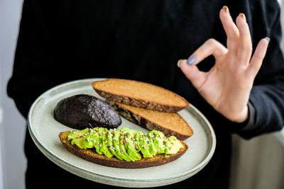 Female hand holding plate with ingredients for healthy avocado toast. ripe hass avocado, wholegrain