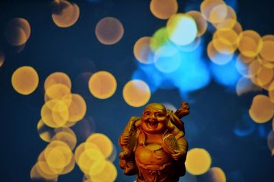 Close-up of buddha statue against lens flares at night