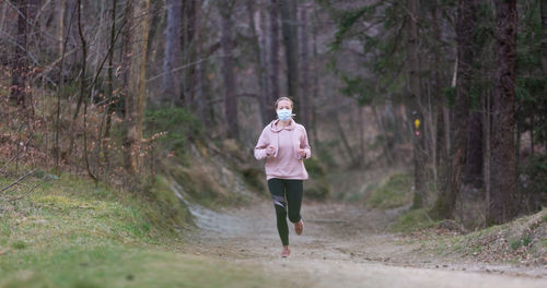 Full length of woman wearing mask running in forest